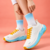 Lammer A002 Sky Blue Woman wearing Lammer A002 white and sky blue running shoes with mustard yellow laces, adjusting her sock against a coral-peach background